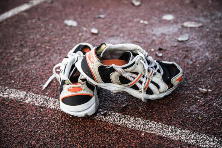 Old worn out running shoes with holes on red running track | Sports Send